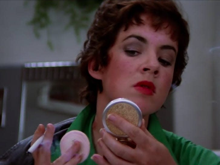 rizzo powdering her face and looking into a compact mirror