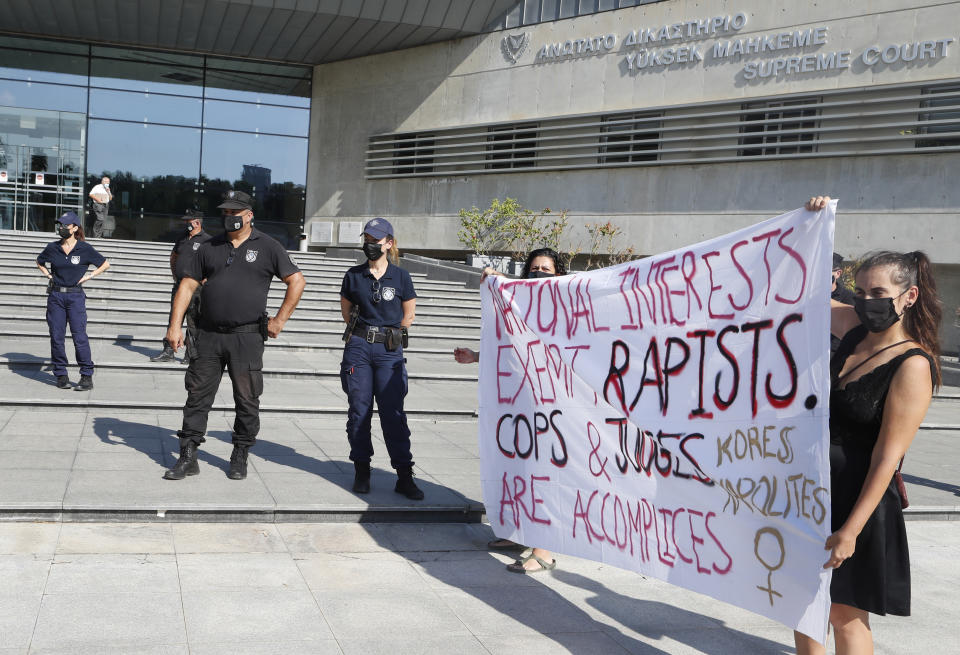 Protesters hold a banner in support of a British woman who is appealing her conviction for making false claims that she was gang raped by as many as a dozen Israelis, as police officers stand guard in front of Cyprus' Supreme Court in the capital Nicosia on Thursday, Sept. 16, 2021. Lawyers for the British woman sentenced to a four-month suspended sentence for making up the gang rape claims during a 2019 Cyprus holiday are appealing to the country's Supreme Court to overturn the conviction. (AP Photo/Philippos Christou)