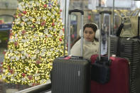 A traveller waits for a train near a large Christmas tree at King's Cross Station in London, Thursday, Dec. 21, 2023. Rail travellers over the Christmas holiday season will have to contend with disruptions to services due to engineering work and bad weather. (AP Photo/Kin Cheung)