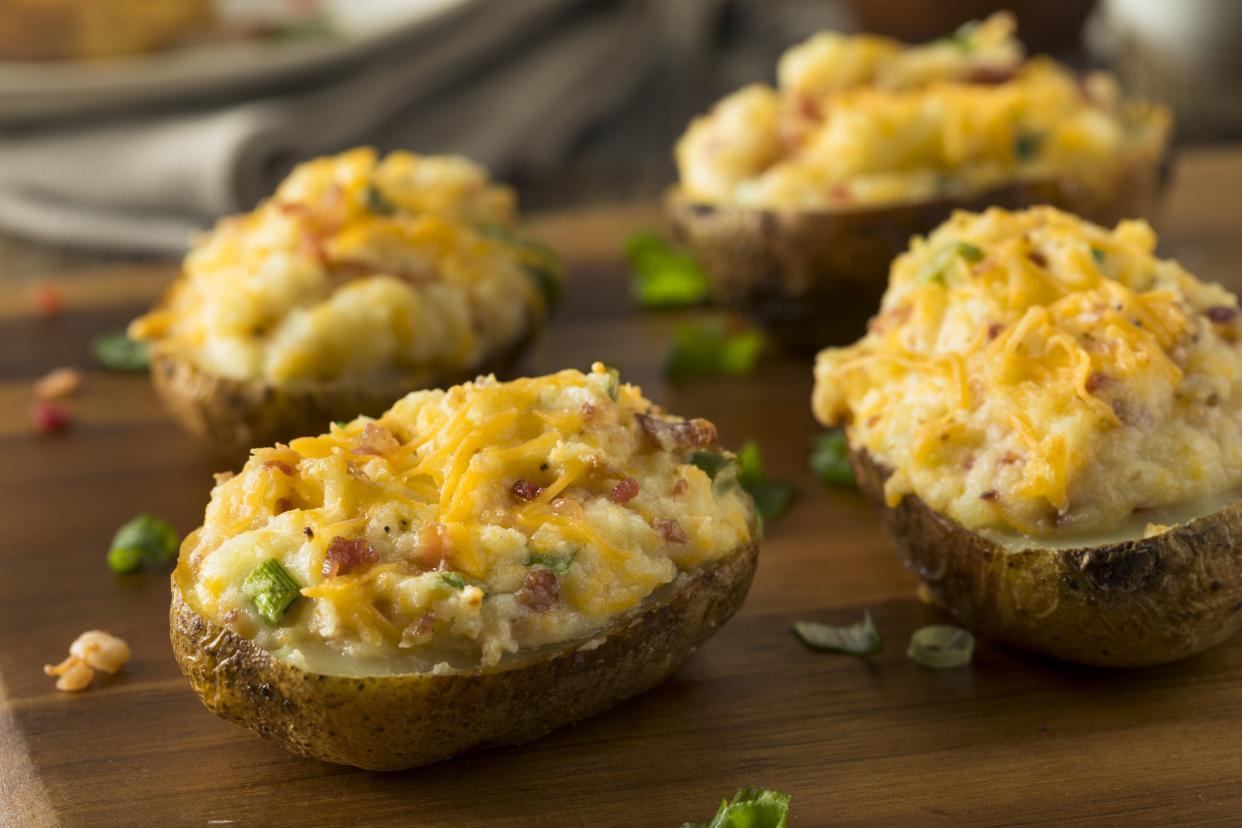 Four broccoli and cheddar-stuffed potato skins with avocado cream on a wooden cutting board with a blurred background