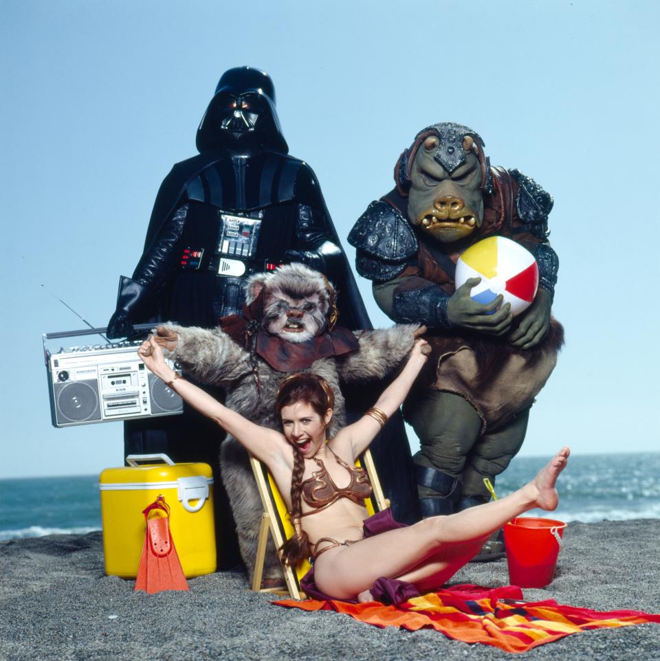 Carrie Fisher posing in the Princess Leia bikini next to Darth Vader, a Gamorrean Guard, and an Ewok.