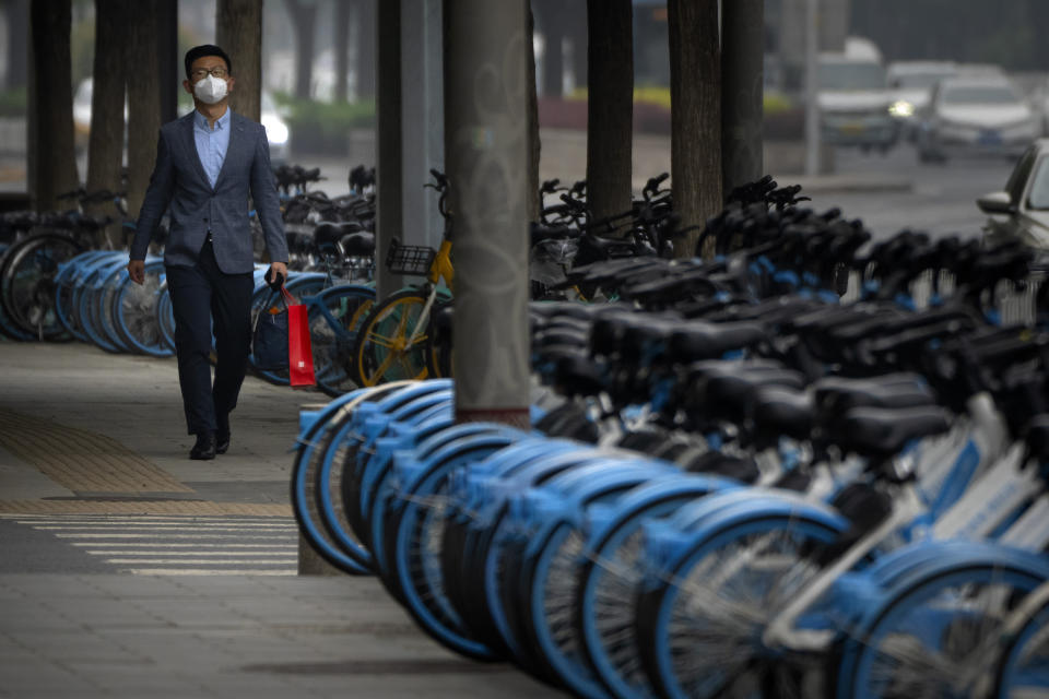 A man wearing a face mask walks past lines of unused share bicycles near a closed subway station in the central business district in Beijing during what is normally the morning rush hour, as most nonessential workers in the district have been ordered to work from home, Tuesday, May 10, 2022. China's capital began another round of three days of mass testing for millions of its residents Tuesday in a bid to prevent an outbreak from growing to Shanghai proportions. (AP Photo/Mark Schiefelbein)