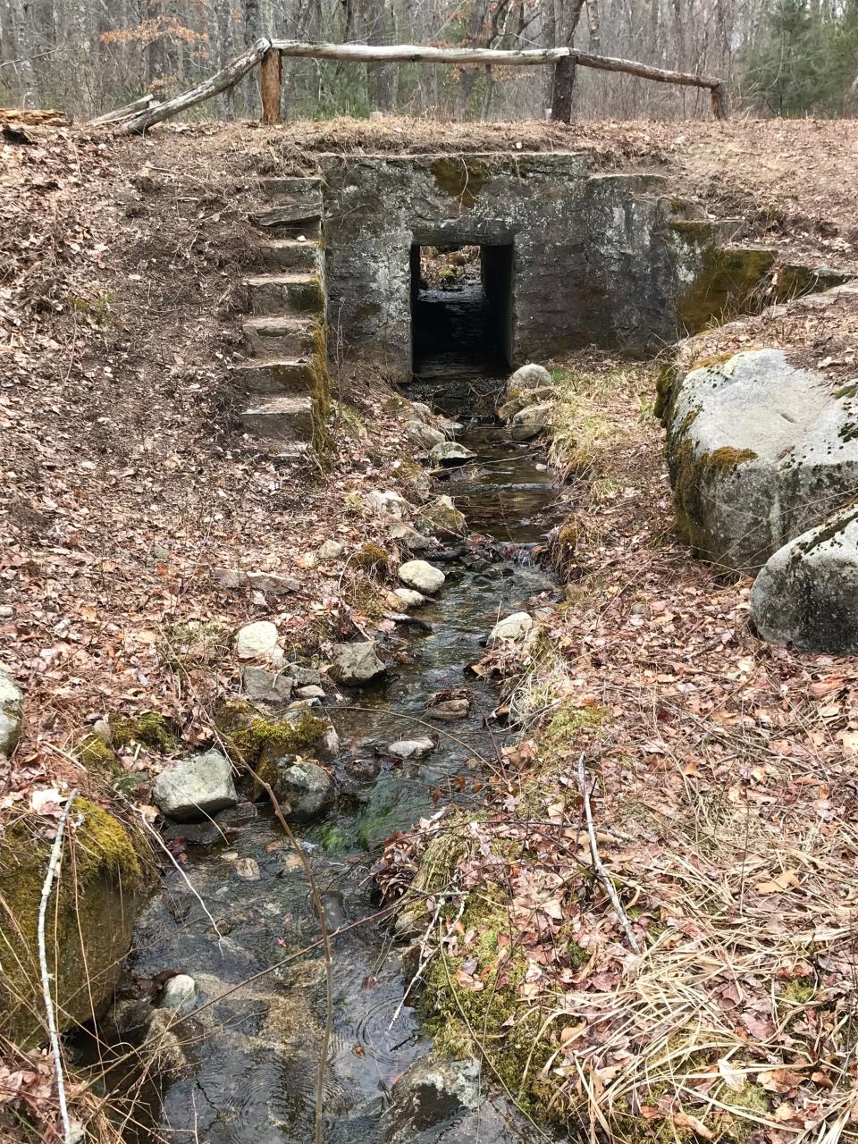 A stream flows through a culvert and under a stone bridge on Plain Road.