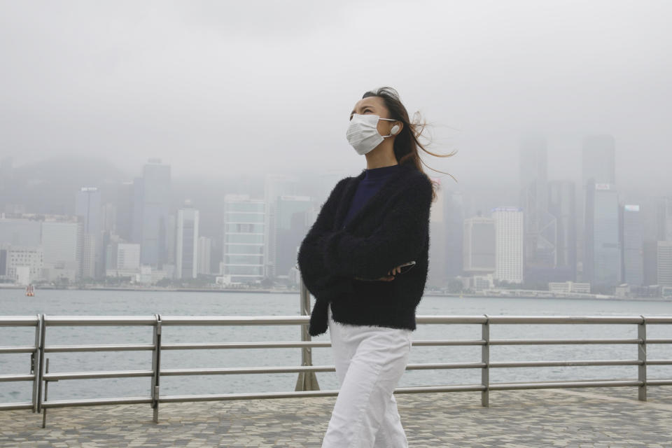 A woman wearing a face mask walks along a street in Hong Kong, Friday, Jan. 28, 2022. Hong Kong is cutting the length of mandatory quarantine for people arriving from overseas from 21 to 14 days, even as the southern Chinese city battles a new surge in COVID-19 cases. (AP Photo/Kin Cheung)