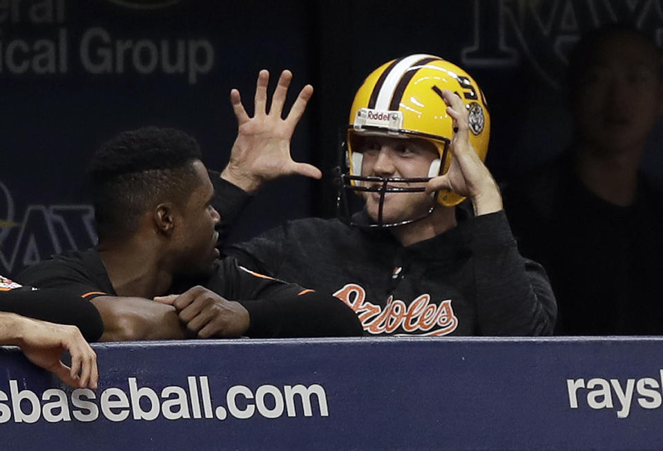Baltimore Orioles relief pitcher David Hess gestures as he wears an LSU football helmet in the dugout during the second inning of the team's baseball game against the Tampa Bay Rays Friday, Sept. 7, 2018, in St. Petersburg, Fla. Hess was hit in the eye with a football while warming up before the game. (AP Photo/Chris O'Meara)