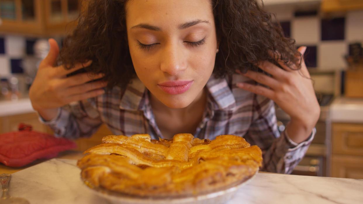 Charming young mixed ethnic woman smelling apple pie in her kitchen.
