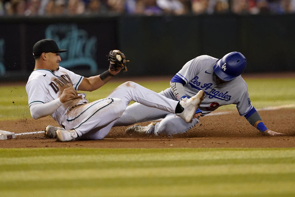 Los Angeles Dodgers' Gavin Lux, right, is caught trying to advance to third by Arizona Diamondbacks' Josh Rojas on a base hit by Mookie Betts during the third inning of a baseball game, Thursday, May 26, 2022, in Phoenix. (AP Photo/Matt York)