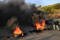 A protester burns tires to block a highway that leads to Beirut's international airport, during a protest against against the economic and financial crisis, in Beirut, Lebanon, Tuesday, March 2, 2021. The Lebanese pound has hit a record low against the dollar on the black market as the country's political crisis deepens and foreign currency reserves dwindle further. (AP Photo/Hussein Malla)