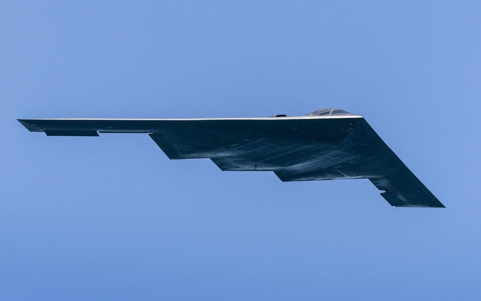 A wedge-shaped stealth bomber is seen against a blue sky