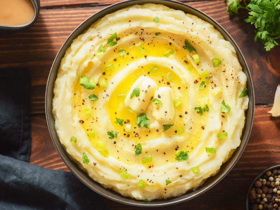 A bowl of creamy mashed potatoes with butter, fresh herbs and freshly cracked black pepper. Top view with close up.