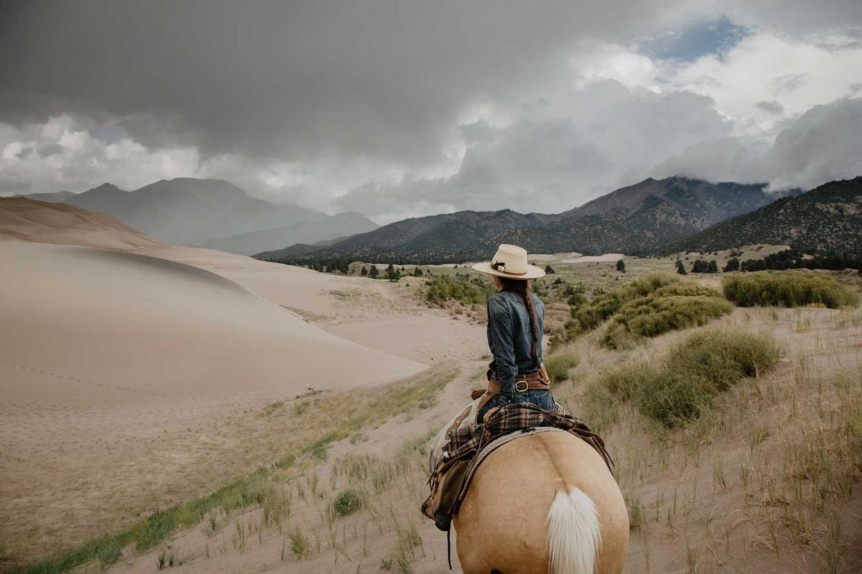 Woman on horseback riding along the sand dunes towards the mountains on a cloudy day