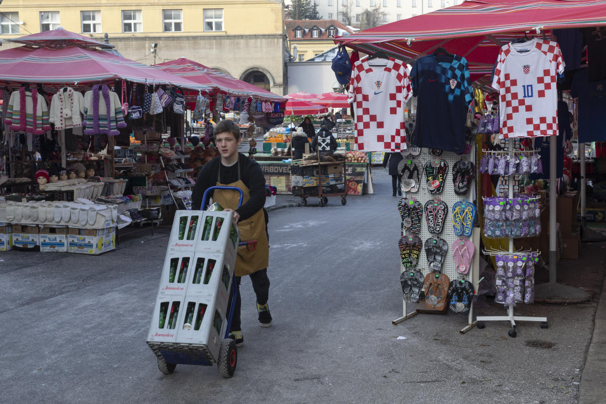A young man pushes a cart past Croatian national soccer team's jerseys on display at a market ahead of the team's Qatar World Cup soccer semifinal match against Argentina, in Zagreb, Croatia, Tuesday, Dec. 13, 2022. (AP Photo/Marko Drobnjakovic)