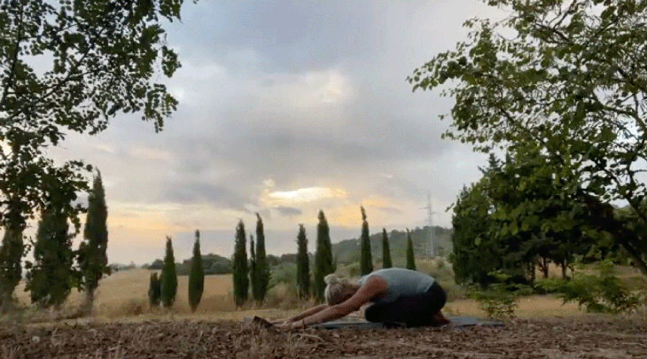 Woman outside on a yoga mat practicing early morning yoga in child's pose