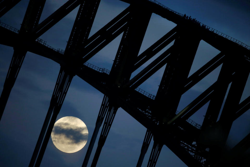 Participants in a Sydney Harbour Bridge Climb walk down the western span of the famous Australian landmark as the supermoon rises through clouds&nbsp;on Monday.