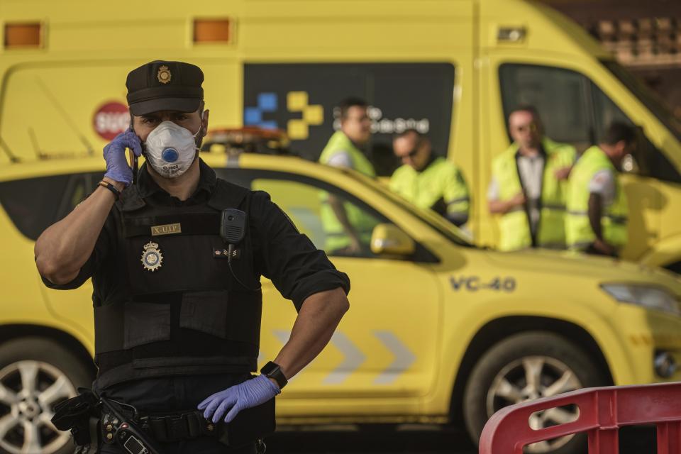 A police officer wearing a mask talks on the phone in front of the H10 Costa Adeje Palace hotel in La Caleta, in the Canary Island of Tenerife, Spain, Wednesday, Feb. 26, 2020. Spanish officials say a tourist hotel on the Canary Island of Tenerife has been placed in quarantine after an Italian doctor staying there tested positive for the COVID-19 virus and Spanish news media says some 1,000 tourists staying at the complex are not allowed to leave. (AP Photo)