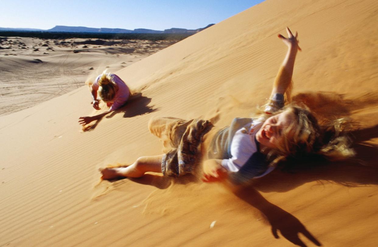 Mother and daughter rolling down sand dunes, Coral Pink Sand Dunes State Park, United States of America
