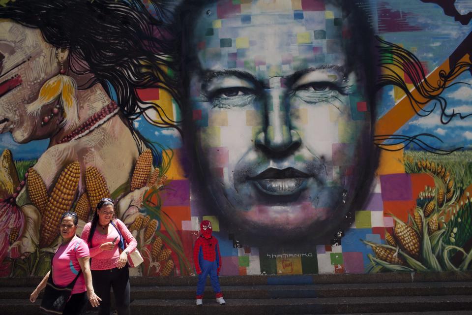 A boy dressed in a Spiderman costume poses for a photo next to a mural of Venezuela's late President Hugo Chavez painted on a wall of the Museo de Bellas Artes in Caracas, Venezuela, Tuesday, March 4, 2014. He’s been dead a year, but Chavez’s face and voice are everywhere. He bangs out the national anthem on state radio every morning and the national guard has even blasted his voice reciting poetry to drive rock-throwing protesters off the street. (AP Photo/Rodrigo Abd)