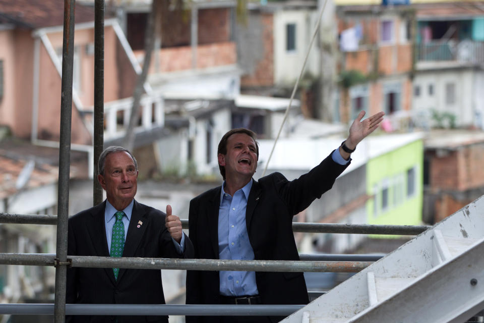 New York Mayor Michael R. Bloomberg, left, and Rio de Janeiro's Mayor Eduardo Paes gesture to construction workers as they visit the Chapeu Mangueira slum during the Rio+C40: Megacity Mayors Taking Action on Climate Change, a parallel event during the UN Conference on Sustainable Development, or Rio+20, in Rio de Janeiro, Brazil, Tuesday, June 19, 2012. While squabbling between rich and poor countries threatens to derail the Earth summit, the world’s mayors say they can’t afford the luxury of endless, fruitless negotiations and are already taking real action to stave off environmental disaster and preserve natural resources for future generations. (AP Photo/Felipe Dana)