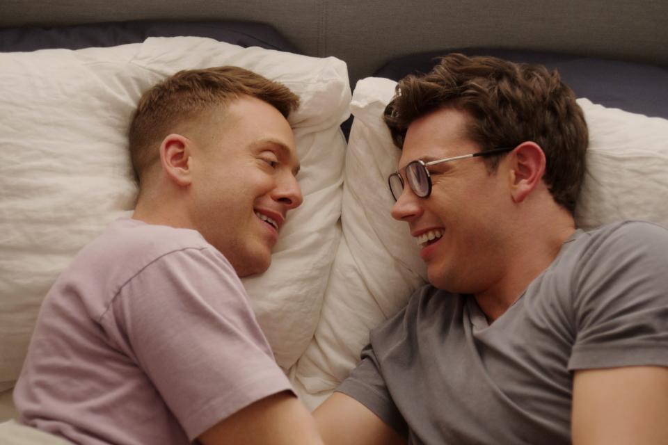Ryan O'Connell and Max Jenkins smile at each other in bed