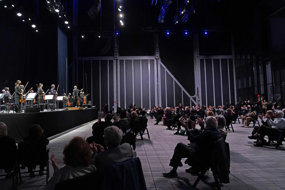 CORRECTS SPELLING OF FIRST NAME TO ESA INSTEAD OF ESSA - A live audience of spectators applauds as members of the New York Philharmonic stand after the orchestra performed a live concert together for the first time since March 10, 2020, at The Shed in Hudson Yards, Wednesday, April 14, 2021, in New York. Esa-Pekka Salonen, music director of the San Francisco Symphony and principal conductor of London's Philharmonia Orchestra, gestures from the stage. (AP Photo/Kathy Willens)