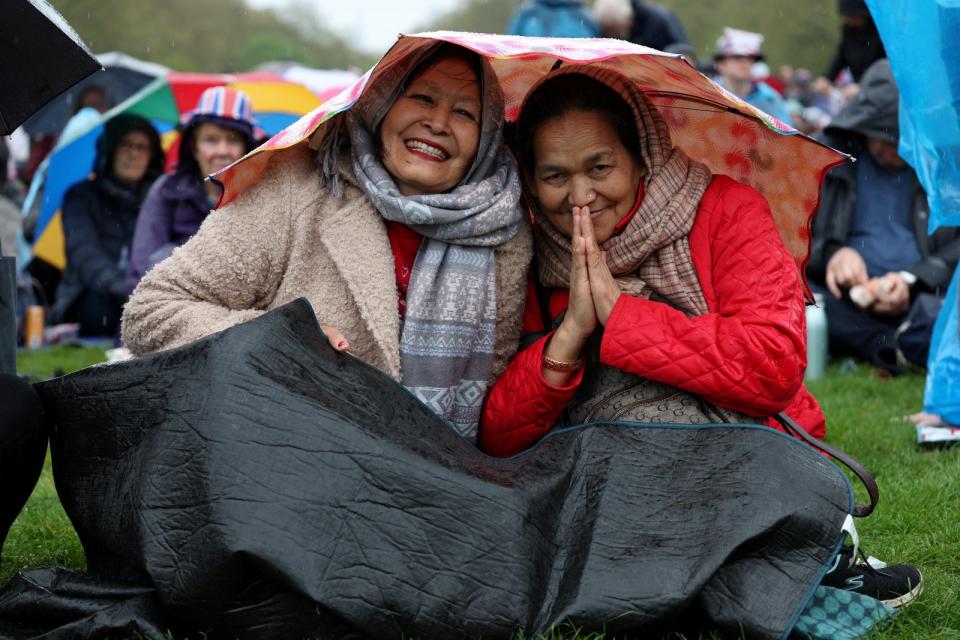 民眾在西敏寺外的草皮一邊用雨傘躲雨，一邊觀看大螢幕上的加冕典禮。路透社
