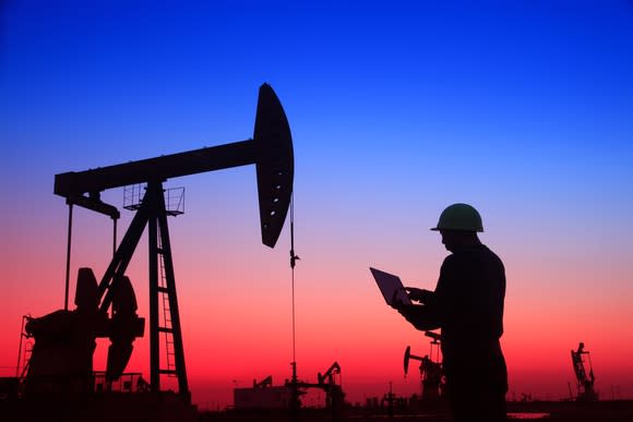 An oil field worker with a laptop at sunset.