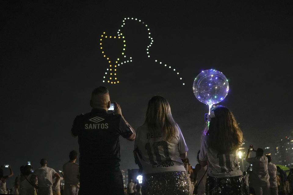 People watch a drone show in homage to the late Brazilian soccer star Pele, over Gonzaga Beach in Santos, Brazil, Saturday, Dec. 31, 2022. Pele, who played most of his career with Santos, died in Sao Paulo on Thursday at the age of 82. (AP Photo/Matias Delacroix)