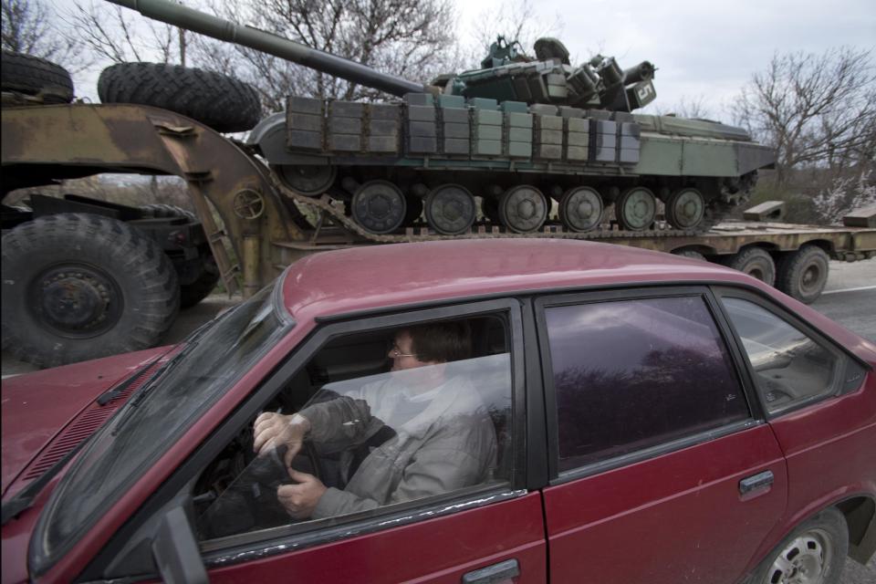 A man drives his car as Ukrainian tanks are transported from their base in Perevalnoe, outside Simferopol, Crimea, Wednesday, March 26, 2014. Ukraine has started withdrawing its troops and weapons from Crimea, now controlled by Russia. (AP Photo/Pavel Golovkin)