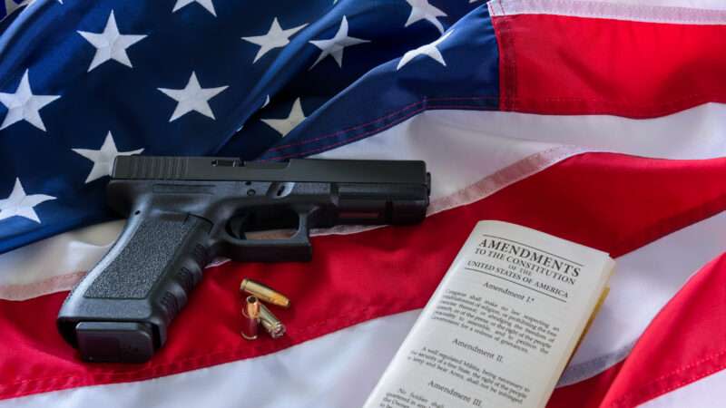 A handgun and a copy of the Constitution against a backdrop of the American flag.