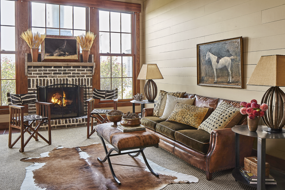 <p>Copper buckets filled with tall wheat stalks flank a framed painting and bring height to this simple mantel arrangement. Pinecone-filled bowls on the ottoman add another natural touch to the den.</p>