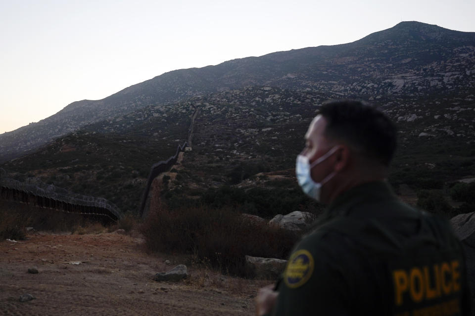 Border Patrol agent Justin Castrejon looks toward where the border wall makes its way over a mountain Thursday, Sept. 24, 2020, near Tecate, Calif. President Donald Trump’s reshaping of U.S. immigration policy may be most felt in his undoing of asylum. Castrejon says migrants pay $8,000 to $10,000 to be guided through the mountains and picked up by a driver once they reach a road. (AP Photo/Gregory Bull)