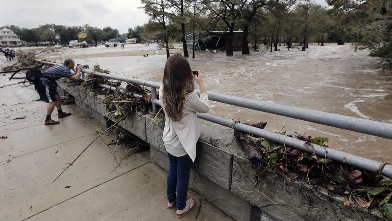 People photograph a swollen Guadalupe River as it sweeps past a debris covered bridge Friday, Oct. 30, 2015, in Gruene, Texas. Storms that day socked an already sodden swath of Texas that was still drying out from the remnants of Hurricane Patricia, forcing evacuations and shutting down a busy 10-mile stretch of interstate.