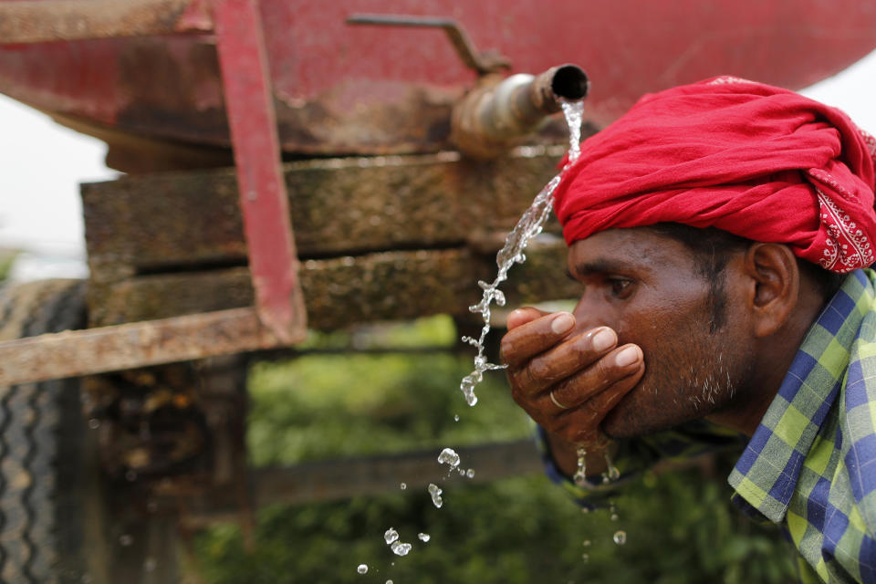 Indian laborer drinks water from a mobile tanker after planting saplings as part of an annual tree plantation campaign on the outskirts of Prayagraj, in northern Uttar Pradesh state, India, Sunday, July 4, 2021. (AP Photo/Rajesh Kumar Singh)
