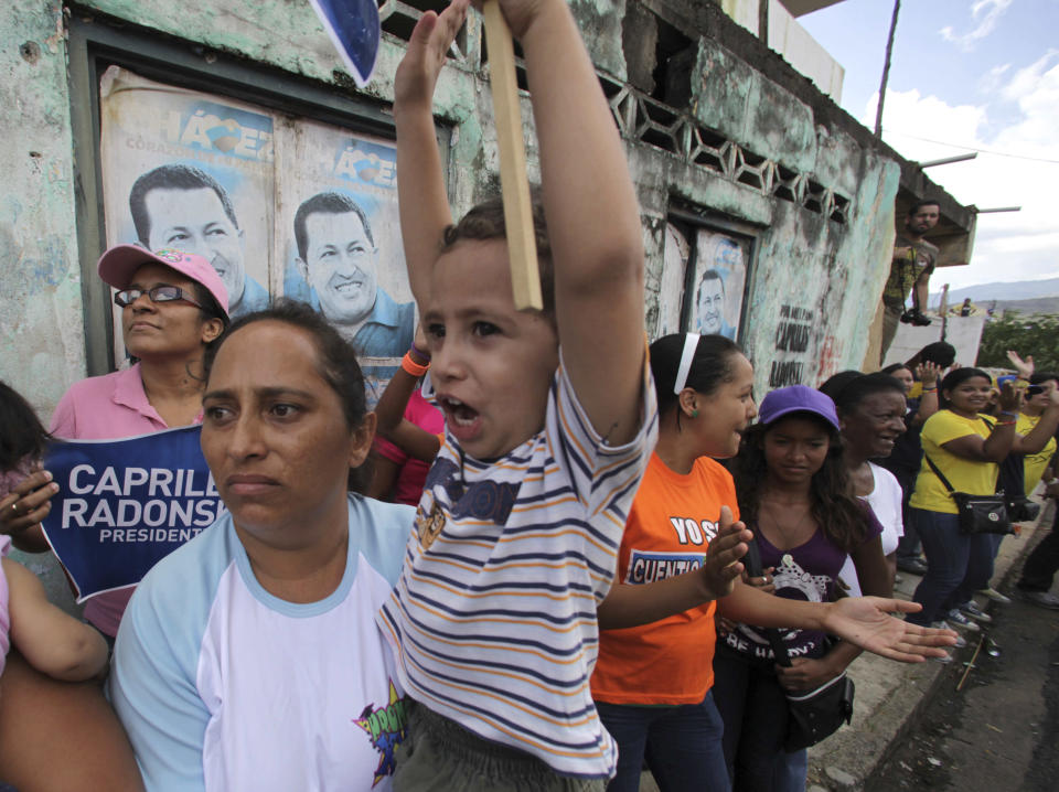 In this Sept. 1, 2012 photo, a woman and her son wait for the arrival of opposition presidential candidate Henrique Capriles as they stand by posters of Venezuela's President Hugo Chavez during a campaign rally for Capriles, in Miranda, Venezuela. From single mothers to construction workers, a segment of President Hugo Chavez supporters have been turning away from the president and instead considering new leadership. They've become key to the Oct. 7 presidential vote and Capriles' strategy. (AP Photo/Fernando Llano)