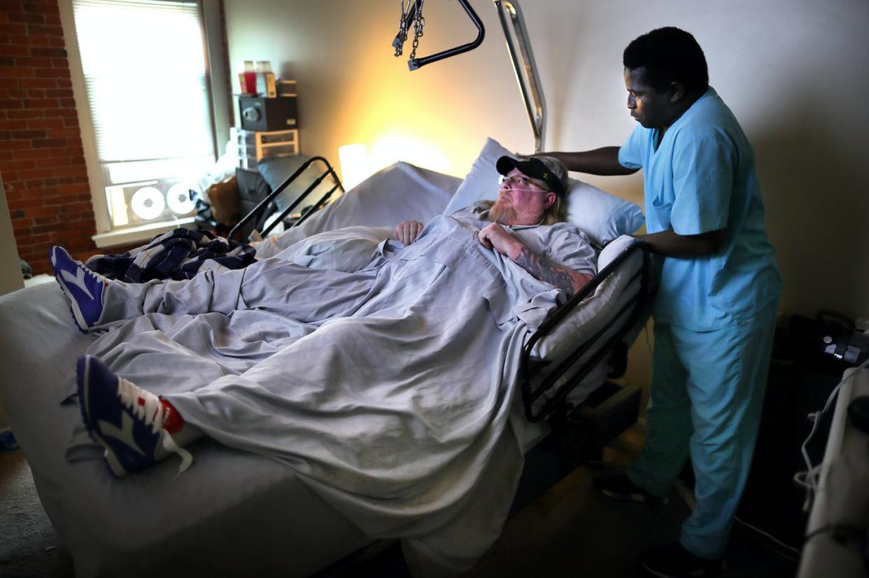 <span class="caption">Home health worker Mass Joof adjusts the pillow for Eric McGuire in Franklin, Mass., on March 25, 2020. </span> <span class="attribution"><a class="link " href="https://www.gettyimages.com/detail/news-photo/mass-joof-adjusts-the-pillow-for-eric-mcguire-who-is-news-photo/1208644550?adppopup=true" rel="nofollow noopener" target="_blank" data-ylk="slk:Photo by John Tlumacki/The Boston Globe via Getty Images;elm:context_link;itc:0;sec:content-canvas">Photo by John Tlumacki/The Boston Globe via Getty Images</a></span>