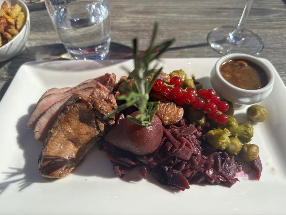 white plate with boar slices, poached pear, chestnuts, red cabbage, and brussels sprouts on a grey table