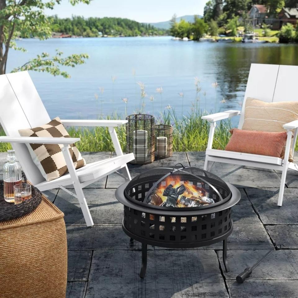 Two outdoor chairs by a fire pit with decorative items on a patio overlooking a lake