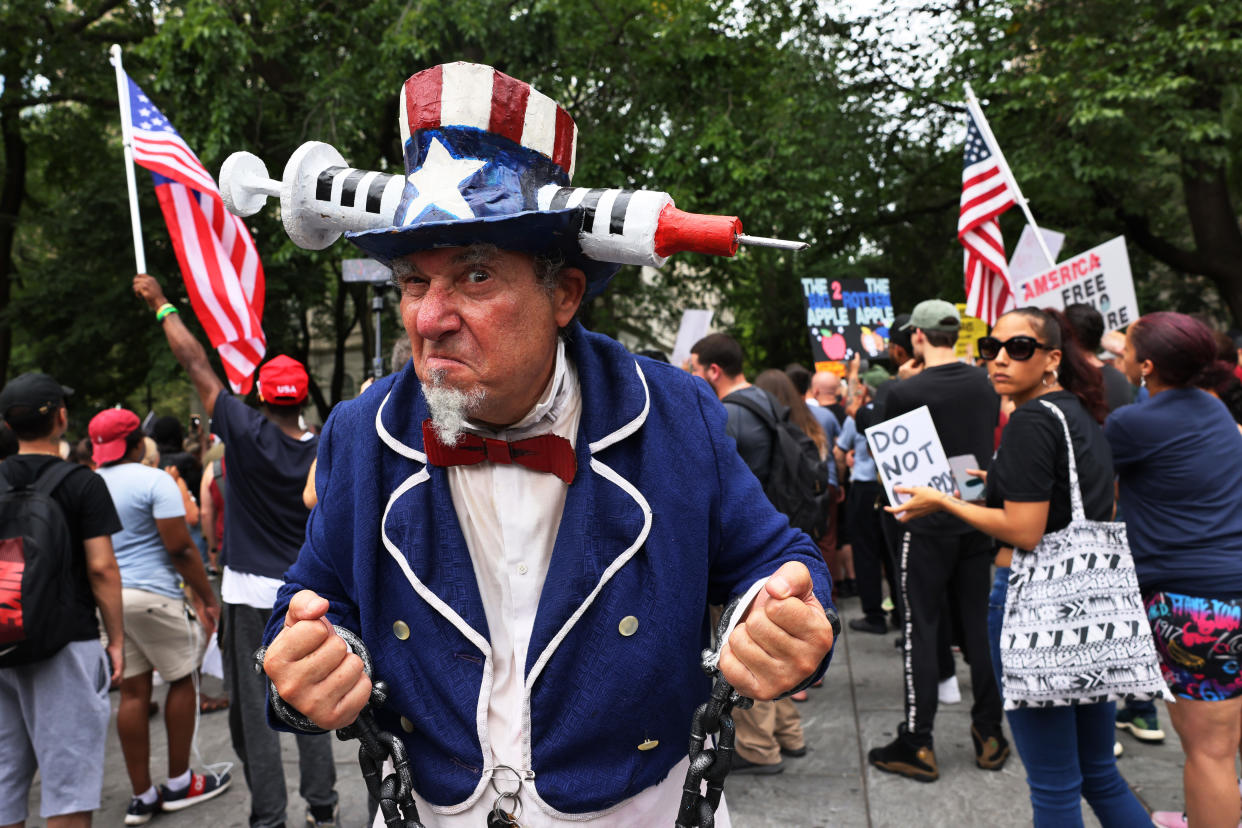People, some carrying American flags and one dressed as Uncle Sam, gather to protest vaccine mandates in New York City. 
