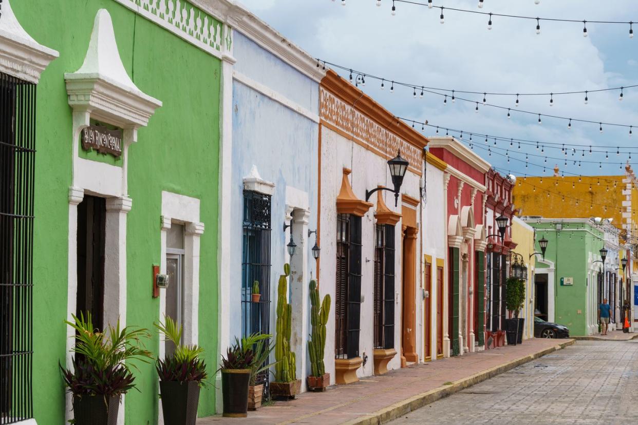 colorful old buildings and potted plants line a narrow street in campeche