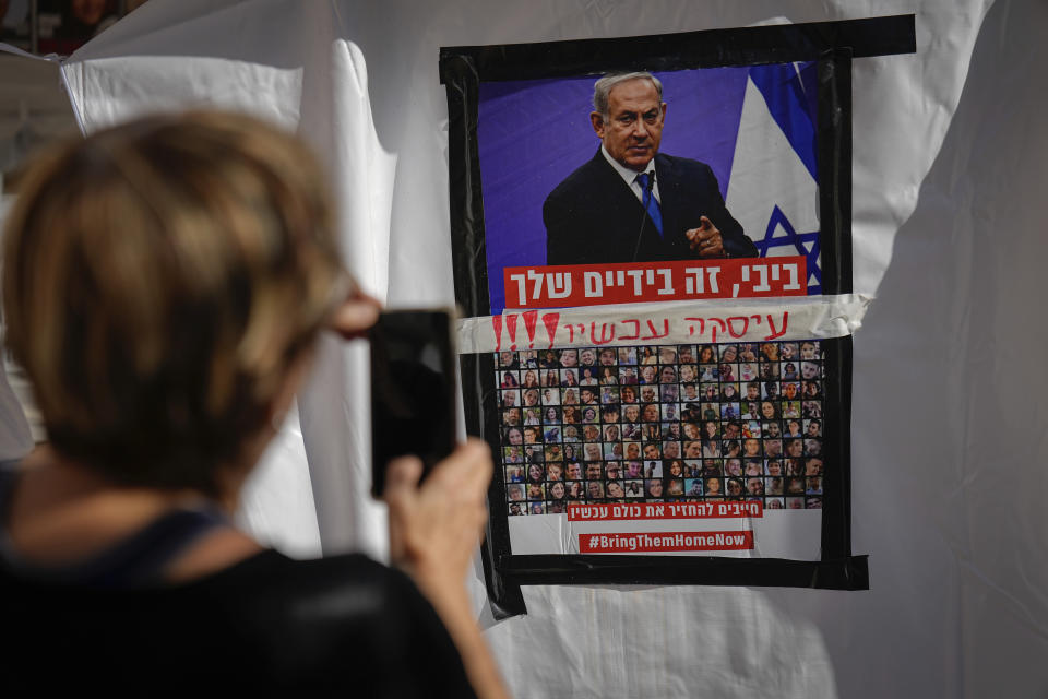 A woman takes a photo of a poster showing Israelis held captive in Gaza plastered underneath a picture of Prime Minister Benjamin Netanyahu with calls for the Israeli leader to reach a deal to bring them home, in Tel Aviv, Israel Tuesday, Nov. 21, 2023. The Hebrew reads, "Bibi, it's in your hands. deal now." The hostages, mostly Israeli citizens, were kidnapped during an Oct. 7 Hamas cross-border attack in Israel and have been held in Gaza since then. (AP Photo/Ariel Schalit)