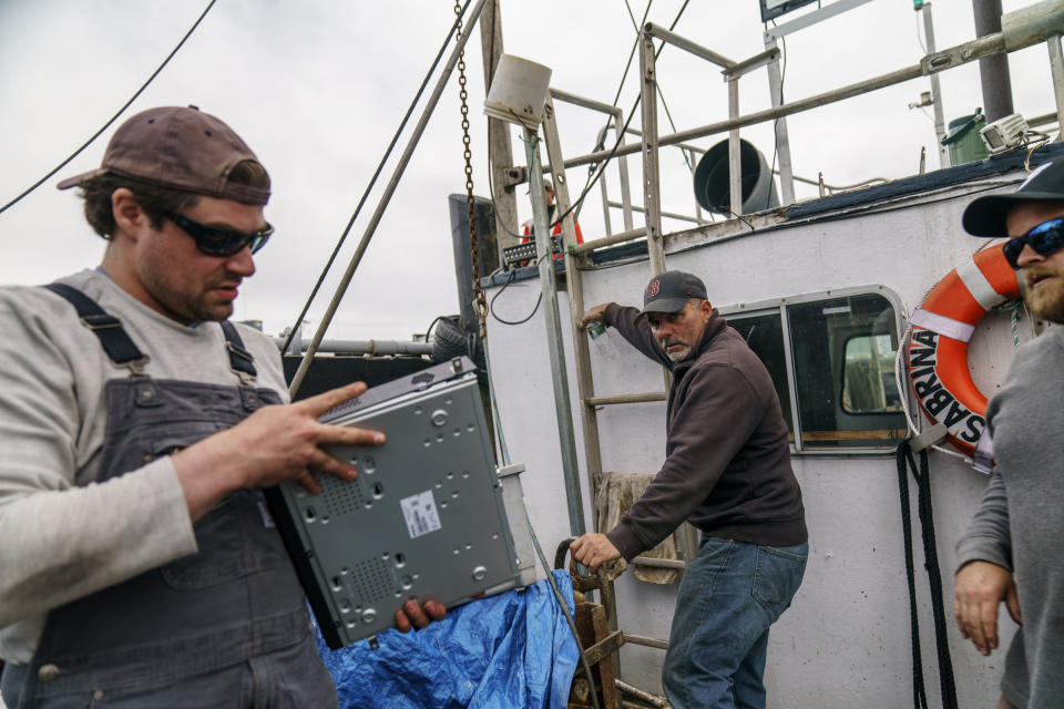 Captain Al Cottone, center, looks on as Mark Hager, right, and Anthony Lucia, install cameras on his fishing boat, the Sabrina Marina, in Gloucester, Mass., Wednesday, May 11, 2022. Hager's Maine-based startup, New England Maritime Monitoring, is one of a bevy of companies seeking to help commercial vessels comply with new federal mandates aimed at protecting dwindling fish stocks. But taking the technology overseas, where the vast majority of seafood consumed in the U.S. is caught, is a steep challenge. (AP Photo/David Goldman)