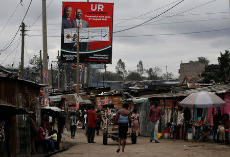 Residents walk below a billboard displaying Kenya's President Uhuru Kenyatta and Deputy President William Ruto from the Jubilee party in Mathare slum, in Nairobi, Kenya, August 15, 2017. REUTERS/Siegfried Modola