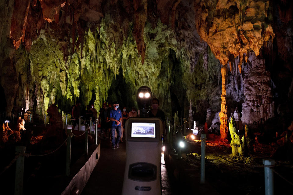 Persephone guides the visitors inside Alistrati cave, about 135 kilometers (84 miles) northeast of Thessaloniki, Greece, Monday, Aug. 2, 2021. Persephone, billed as the world's first robot used as a tour guide inside a cave, has been welcoming visitors to the Alistrati cave, since mid-July. (AP Photo/Giannis Papanikos)