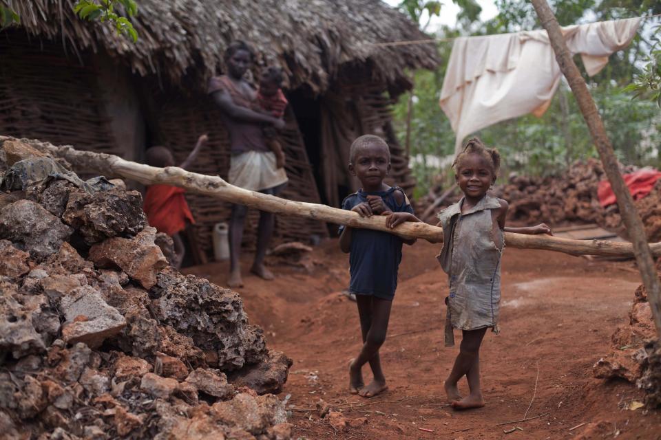 In this Tuesday, March 25, 2014 photo, Jeannes Beltinor, 5, left center, and his 3-year-old sister Katinaeil, stand outside their home in Bombardopolis, northwestern Haiti. “When they were born they looked like real kids, healthy, but as they’ve grown up they’ve started to look unhealthy,” said Jenilia Jean-Baptiste, the children's mother who is pictured in the background. (AP Photo/Dieu Nalio Chery)