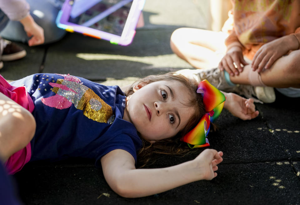 Scarlett Rasmussen, 8, lies underneath a play structure during recess at Parkside Elementary School Wednesday, May 17, 2023, in Grants Pass, Ore. Chelsea Rasmussen has fought for more than a year for her daughter, Scarlett, to attend full days at Parkside and says school employees told her the district lacked the staff to tend to Scarlett’s medical and educational needs, which the district denies. Scarlett is nonverbal and uses an electronic device and online videos to communicate, but reads at her grade level. She was born with a genetic condition that causes her to have seizures and makes it hard for her to eat and digest food, requiring her to need a resident nurse at school. (AP Photo/Lindsey Wasson)