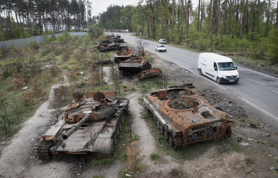 Cars pass by destroyed Russian tanks in a recent battle against Ukrainians in the village of Dmytrivka, close to Kyiv, Ukraine, Monday, May 23, 2022. No matter where Ukrainians live, the 3-month-old war never seems to be far away. Those in towns and villages near the front lines hide in basements from constant shelling, struggling to survive with no electricity or gas — and often no running water. (AP Photo/Efrem Lukatsky)