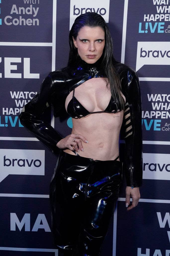 Julia poses on a red carpet with her hand on her hip. She's wearing a leather bikini top and matching pants along with a matching bolero