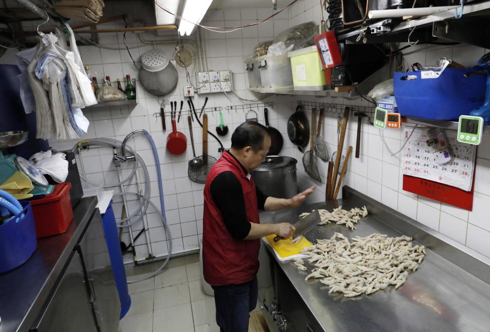 In this Monday, Jan. 23, 2017 photo, chicken feet snacks shop owner Leung Kin-kung chops off chicken feets in Hong Kong. Saturday marks the start of the lunar Year of the Rooster and families in China will reunite for festivities, fireworks and food. While tradition calls for feasting on “auspicious” foods, many will also munch on staple snacks like “phoenix claws,” the Chinese name for chicken feet. (AP Photo/Vincent Yu)