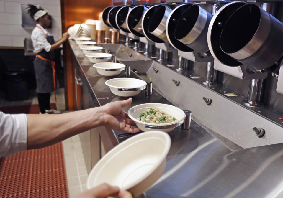 FILE- In this May 3, 2018, file photo a worker lifts a lunch bowl off the production line at Spyce, a restaurant which uses a robotic cooking process, in Boston. Robots aren’t replacing everyone, but a quarter of U.S. jobs will be severely disrupted as artificial intelligence accelerates the automation of today’s work, according to a new Brookings Institution report published Thursday, Jan. 24, 2019. (AP Photo/Charles Krupa, File)