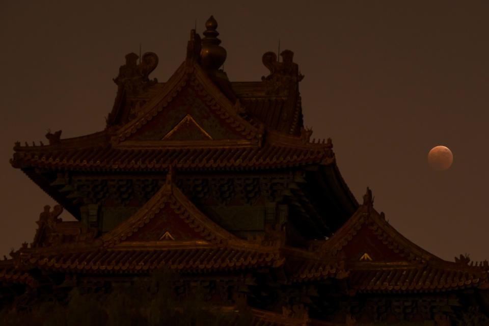 The moon rises behind a corner tower along the outer walls of the Forbidden City during a lunar eclipse in Beijing, Tuesday, Nov. 8, 2022.